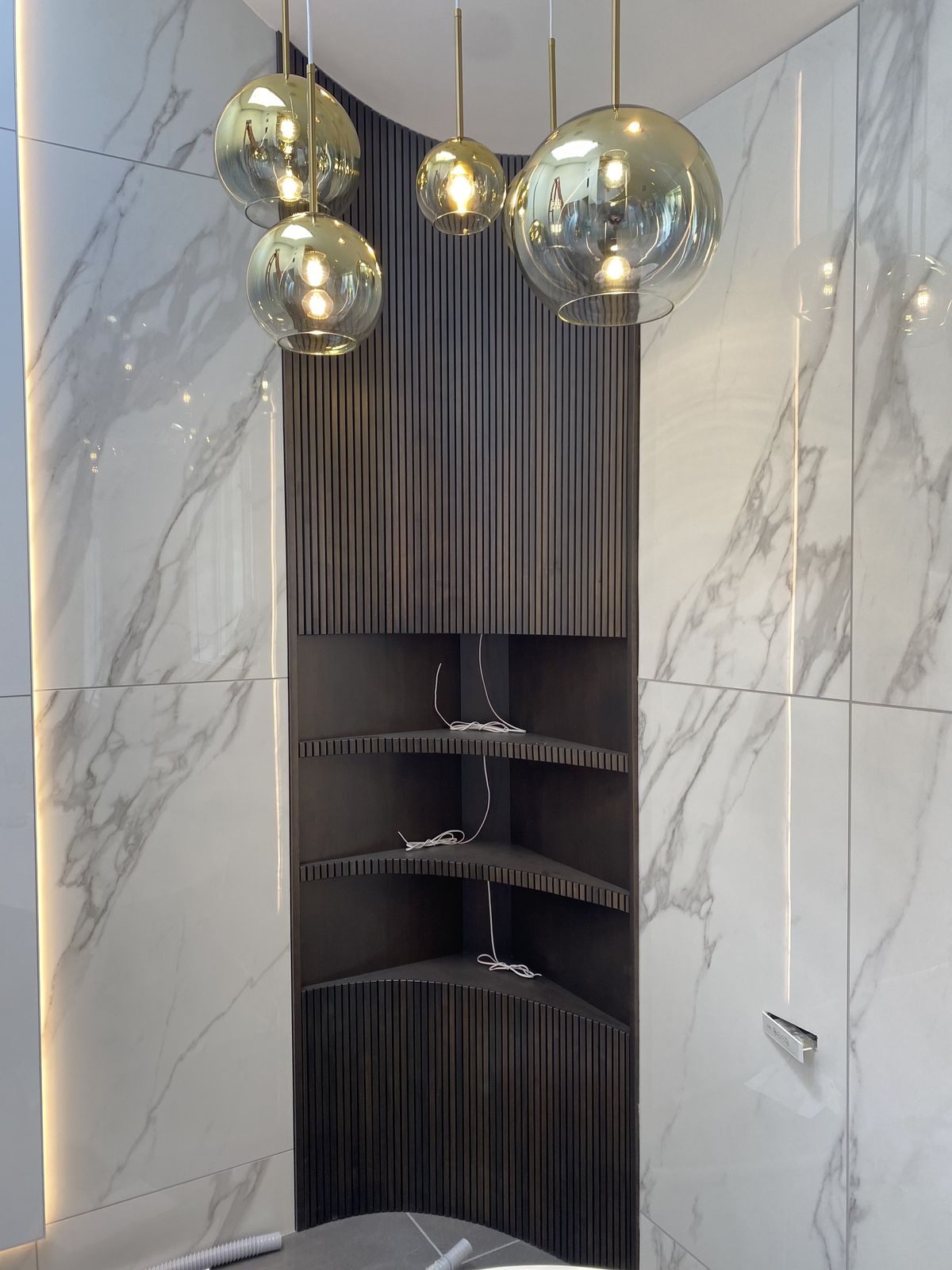Marble bath with fluted dark corner shelving and globe pendants